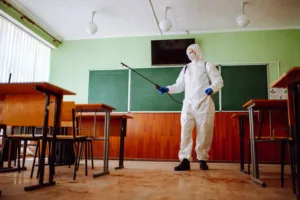 Personne en combinaison de protection désinfectant une salle de classe.