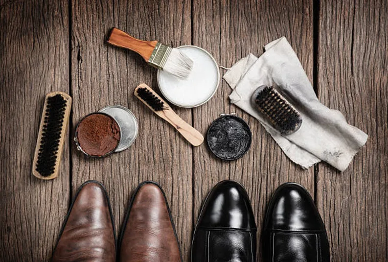 leather boots with shoe maintenance set Ensemble de produits et accessoires pour l'entretien de chaussures en cuir grâce à la terre de Sommières sur une table en bois.