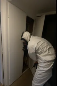 Exterminateur de chez punaises expert vêtu d'une combinaison de protection inspectant un placard pour une infestation de punaises de lit.
