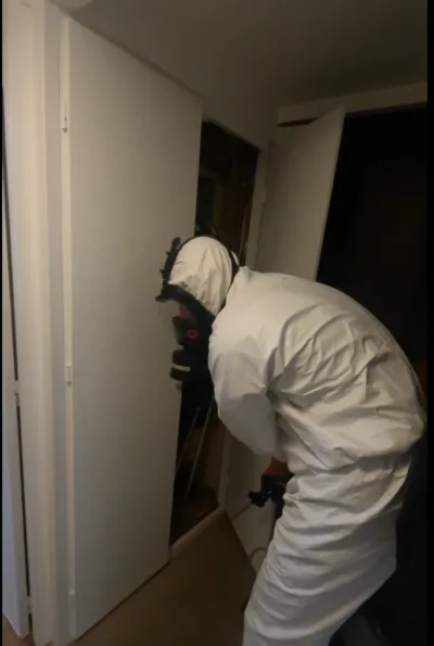Exterminateur de chez punaises expert vêtu d'une combinaison de protection inspectant un placard pour une infestation de punaises de lit.