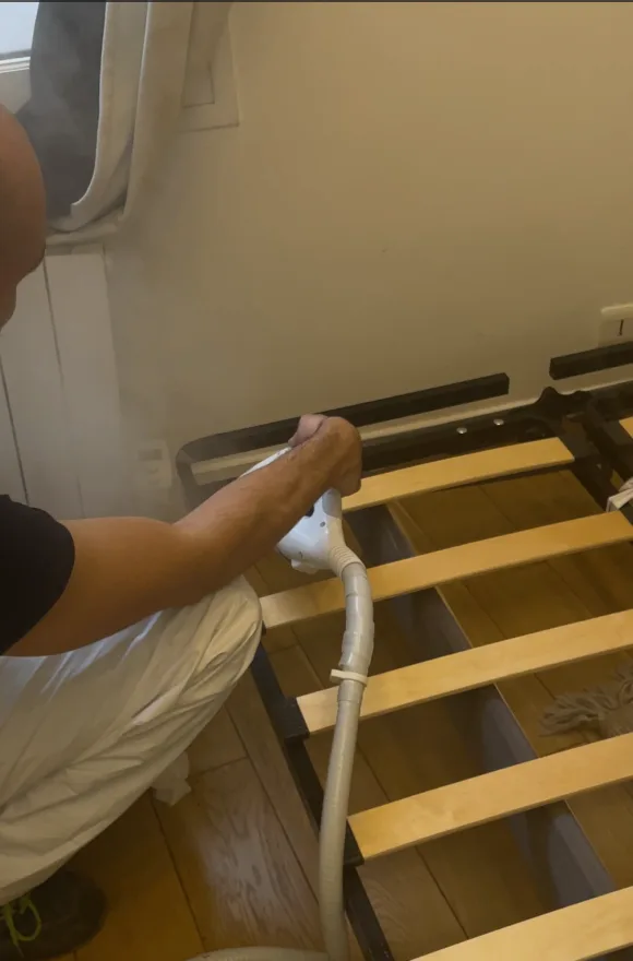 Nettoyage à la vapeur d'un sommier en bois pour traiter une infestation de punaises de lit.