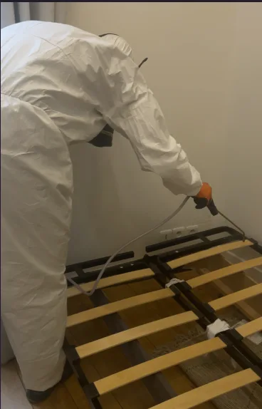Technicien professionnel appliquant un traitement contre les punaises de lit sur un sommier.