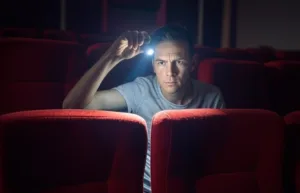 Un homme utilise une lampe de poche pour inspecter des sièges rouges dans une salle de cinéma à la recherche de punaises de lit.