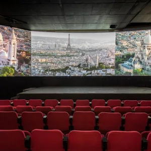 Salle de cinéma avec un grand écran projetant des images de Paris, vue depuis des sièges rouges vides.