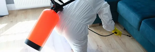 Technicien en combinaison désinfectant un appartement avec un pulvérisateur professionnel.
