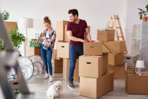 Couple emballant des cartons de déménagement avec leur chien dans une pièce lumineuse.