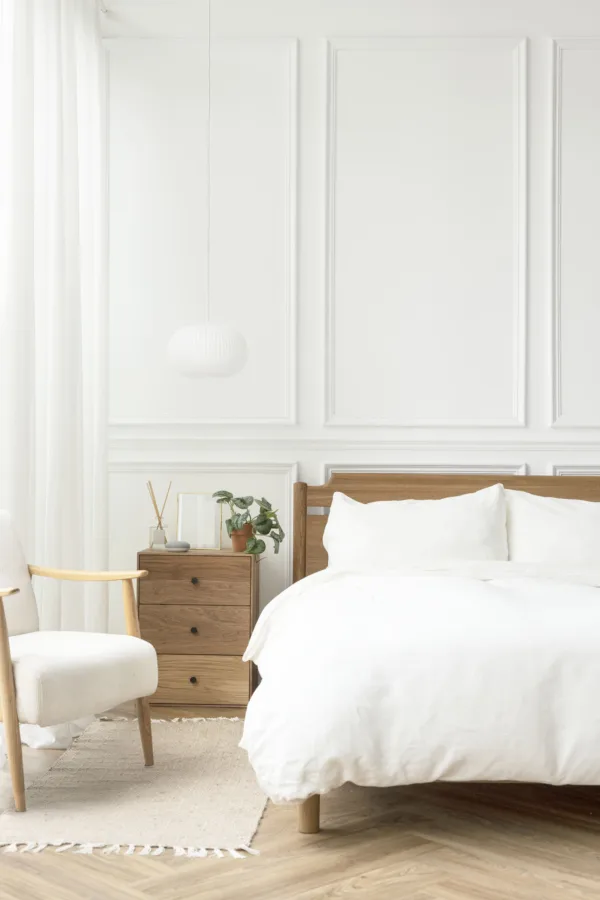 Chambre lumineuse avec lit blanc et mobilier en bois, illustrant les endroits où peuvent se cacher les punaises de lit.